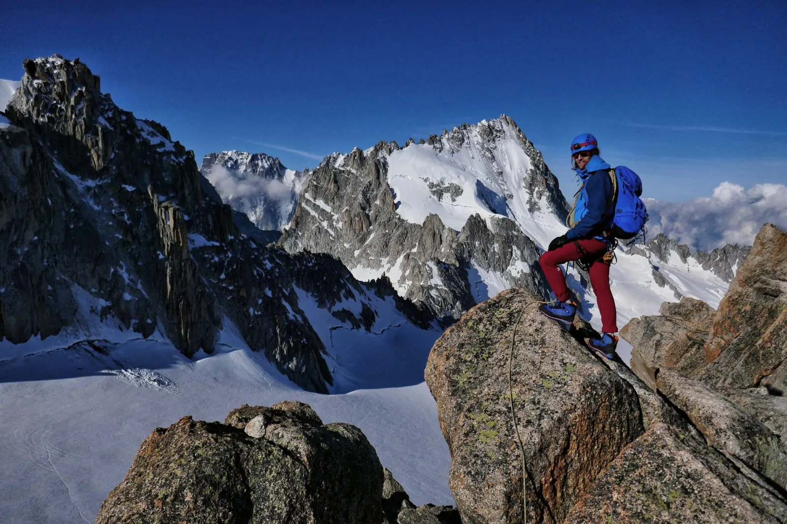 Julien debout sur un rocher de granit, face aux aiguilles enneigées