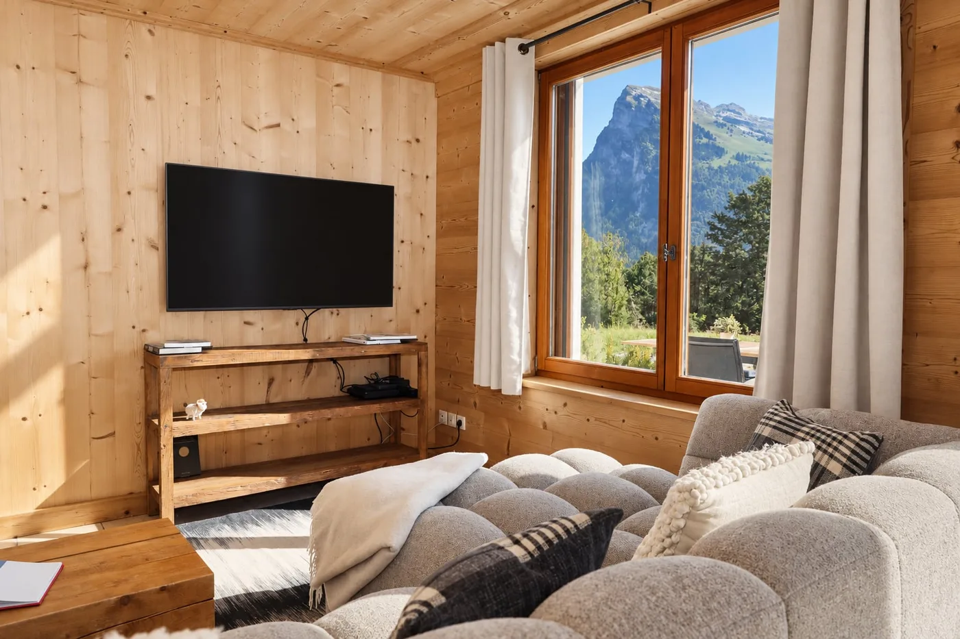 Salon en bois clair, canapé et fenêtre ouverte sur la montagne